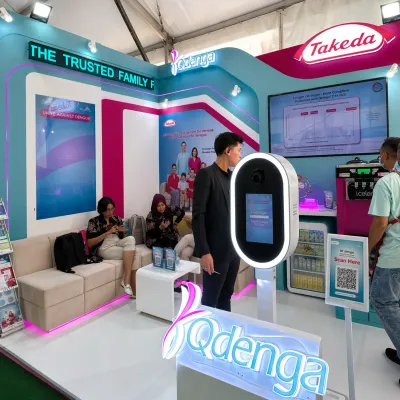 Interactive touchscreen presentation system inside the Takeda Qdenga event booth with digital display and product information area