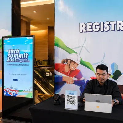 Digital registration system setup for SRM Summit Pertamina 2025 with QR code scan instruction, scanner device, and operator dashboard at the check-in desk