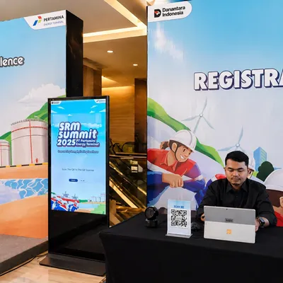 SRM Summit Pertamina 2025 registration area featuring branded digital signage, QR code scanner, and operator desk for guest check-in and souvenir validation